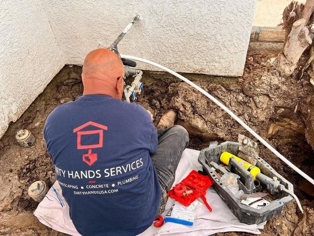 Plumber repairing outdoor plumbing at site, tools and materials organized nearby.
