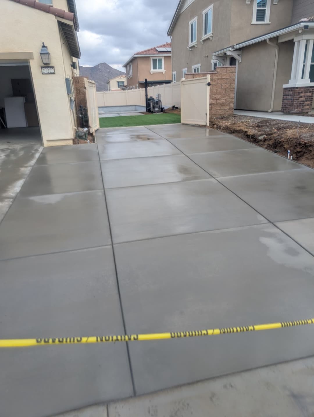 Freshly poured concrete driveway with caution tape, unfinished landscaping in a residential area.