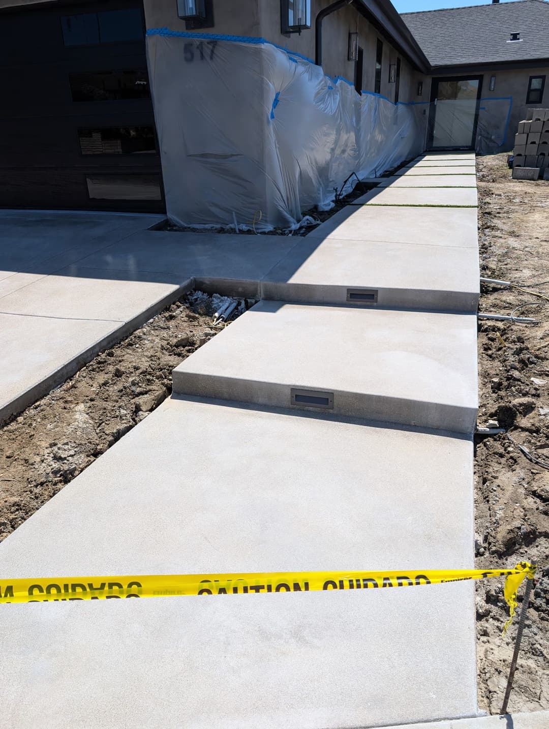Concrete walkway under construction with caution tape in front of a modern home.