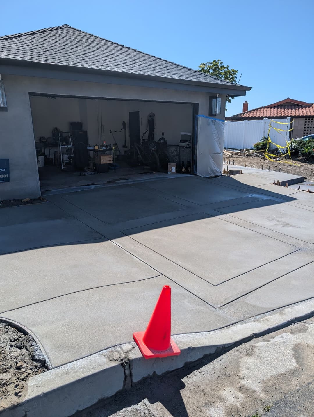 Freshly poured concrete driveway with orange traffic cone near a garage entrance. Clear blue sky.