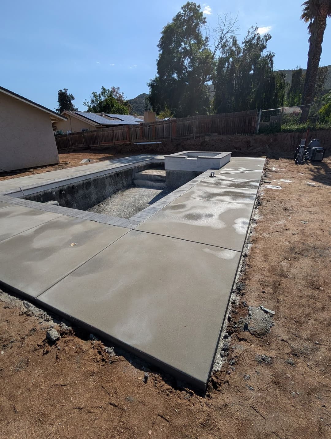Concrete pool construction site with unfinished structure and surrounding landscaping.