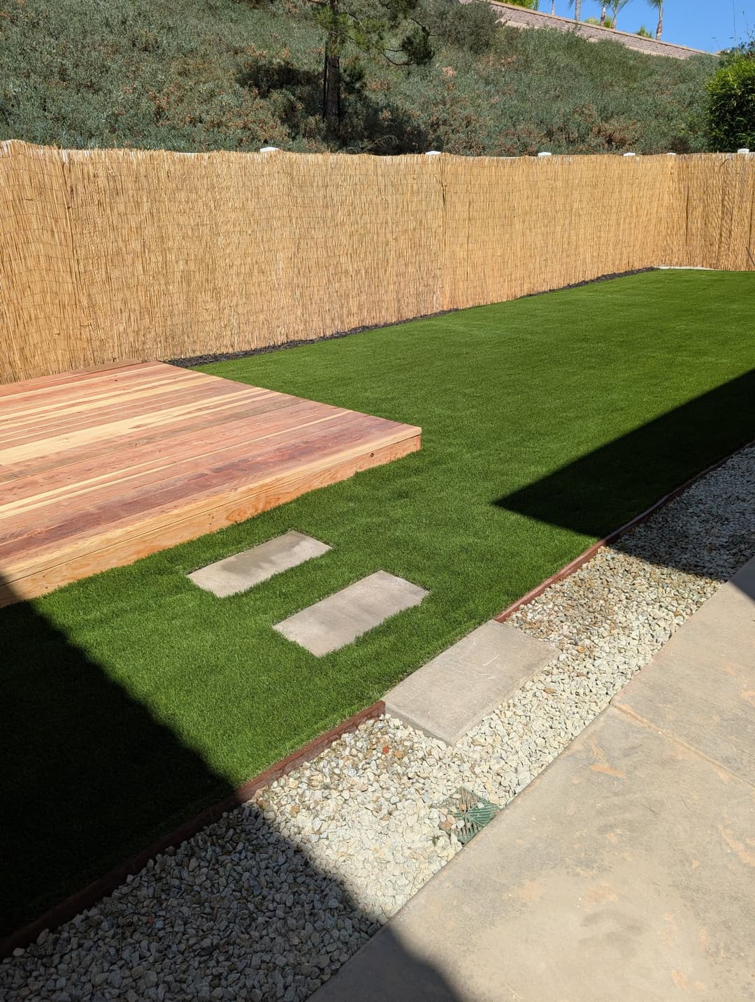 Backyard landscaping featuring artificial grass, wood deck, and stone pathway. Ideal outdoor space.