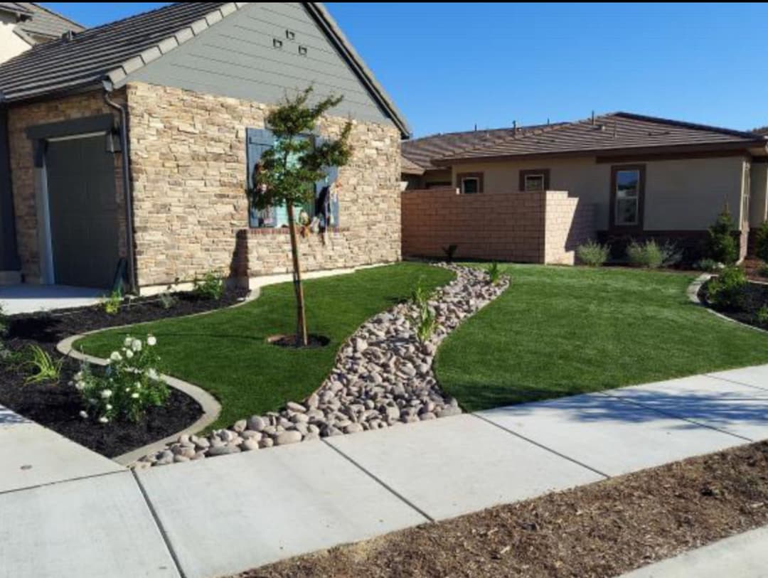 Landscaped front yard with stone path, grass, and flowering plants near a modern home.
