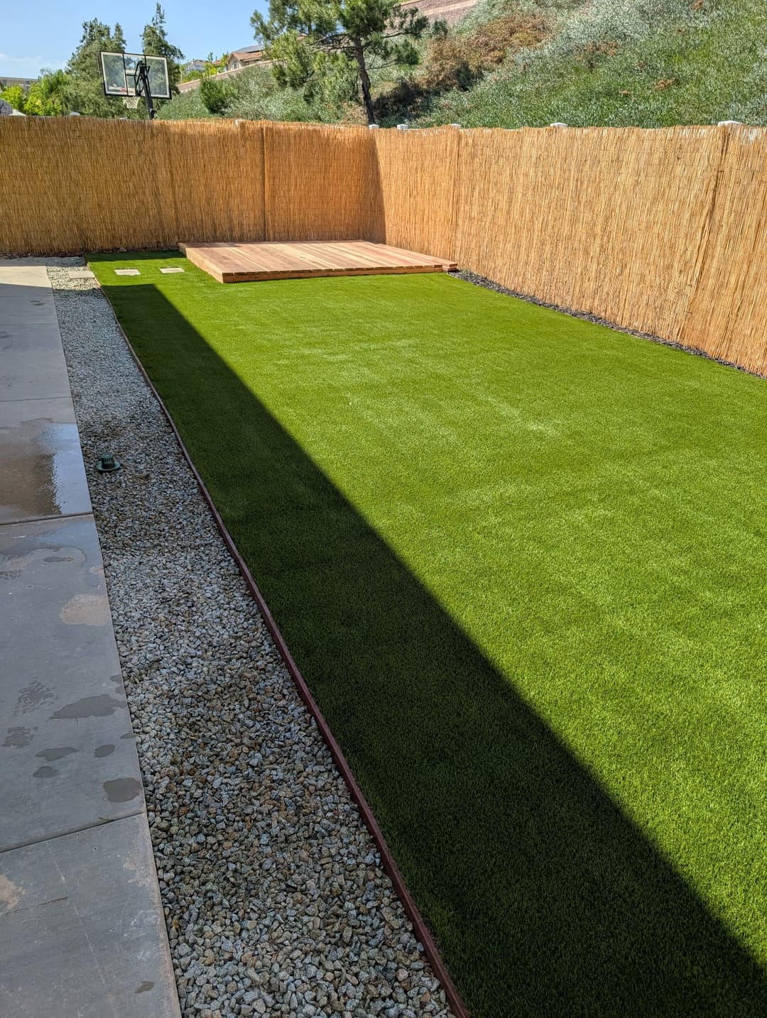 Artificial turf lawn with gravel border and wooden deck in a residential backyard.