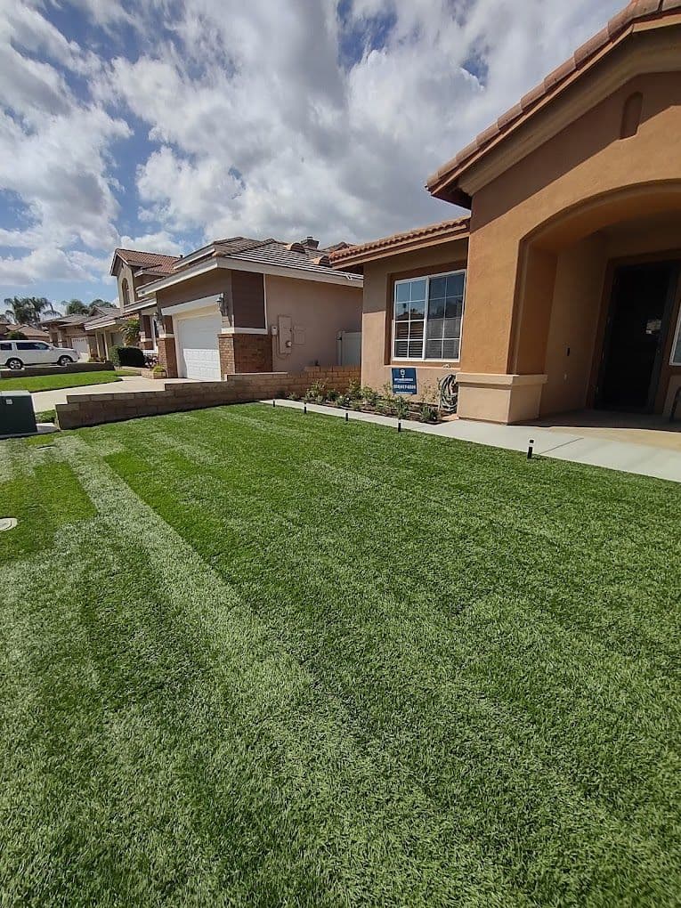 Well-maintained lawn with lush green grass in front of a suburban home and clear blue sky.
