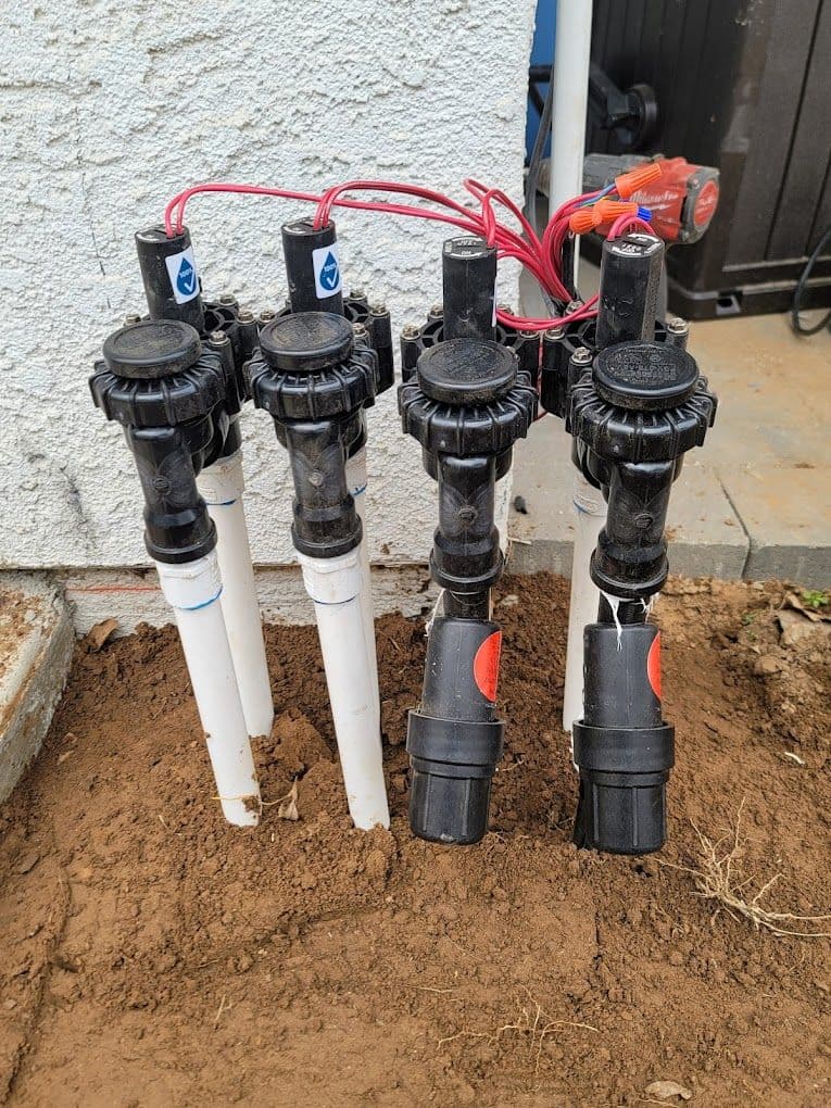 Irrigation valves with wiring and PVC pipes installed in soil for landscaping.