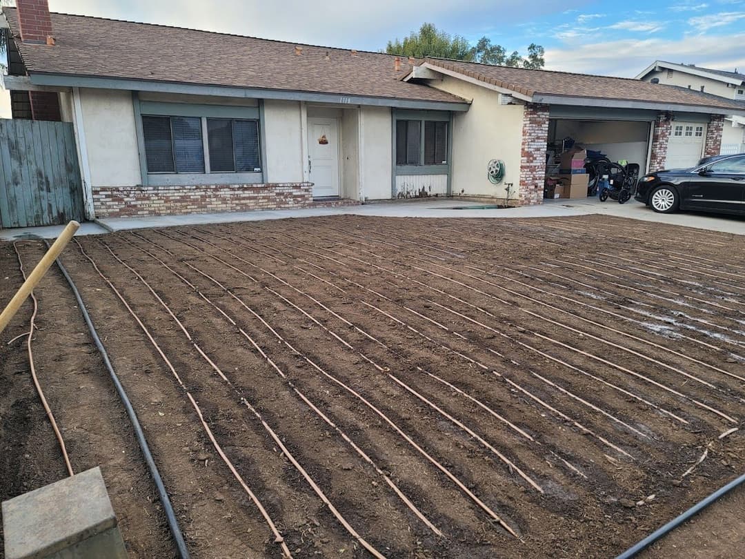 Residential front yard with newly installed irrigation hoses on prepared soil for landscaping.