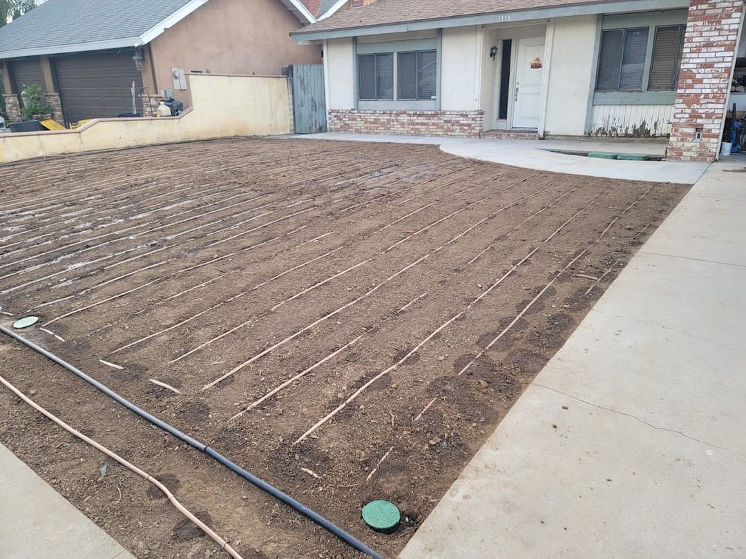 Prepared dirt yard with irrigation lines ready for landscaping in front of a house.