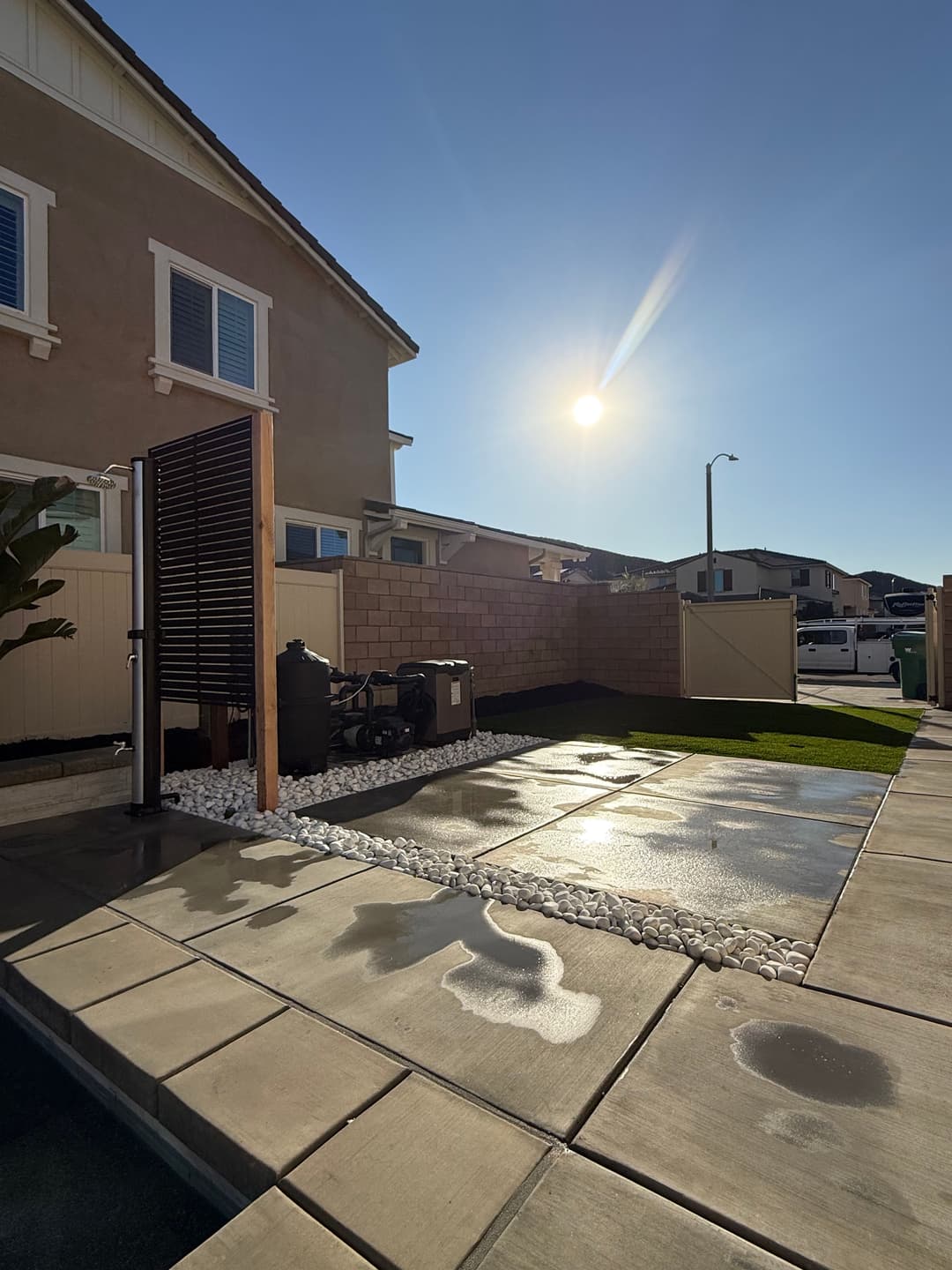 Modern backyard featuring a shower, decorative stones, and a sunny sky.