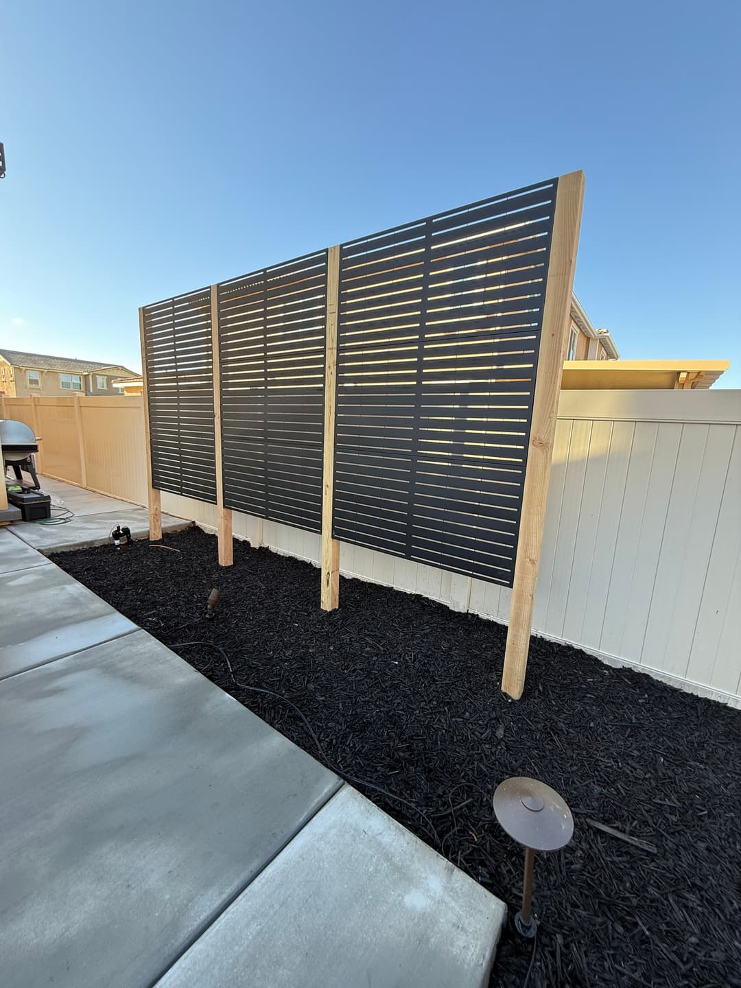 Modern slatted wooden privacy screen in landscaped yard with mulch and outdoor lighting.