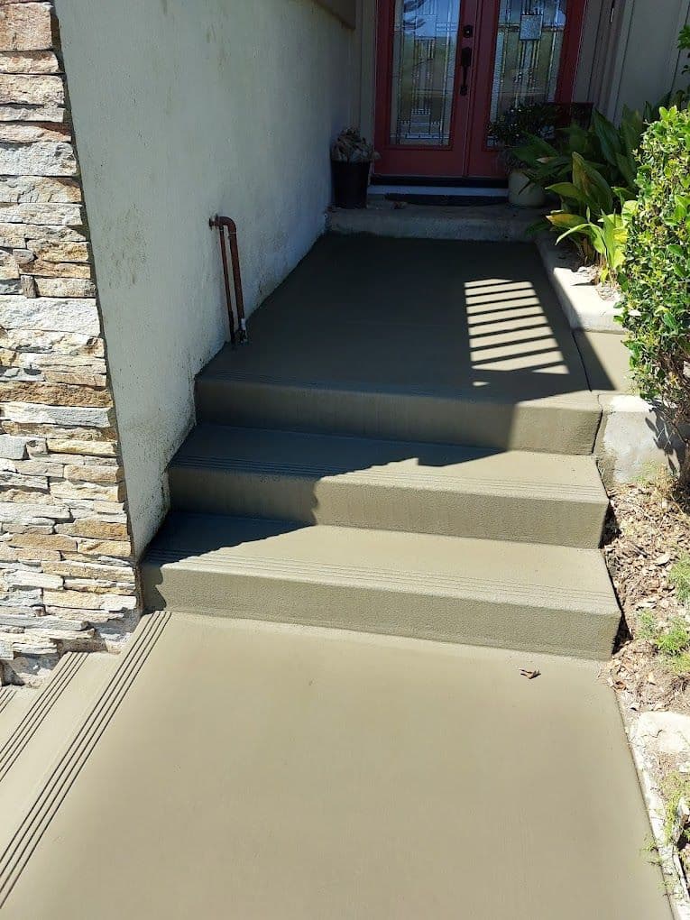 Newly poured concrete steps leading to a front door, surrounded by greenery and decorative stone.
