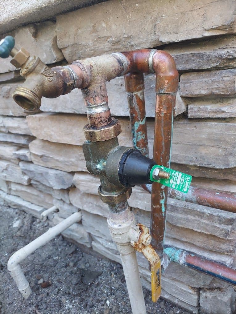 Bronze water valve and copper pipes installed on a stone wall, showing corrosion.