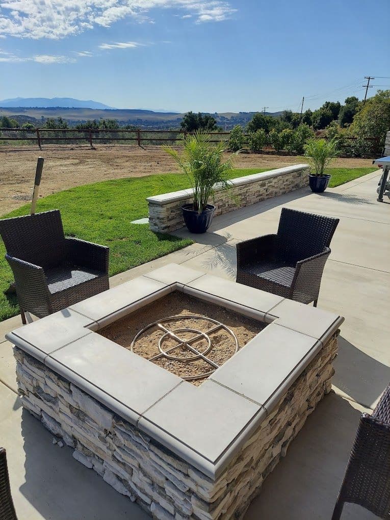 Outdoor patio with a stone fire pit, chairs, and scenic mountain view under a clear sky.
