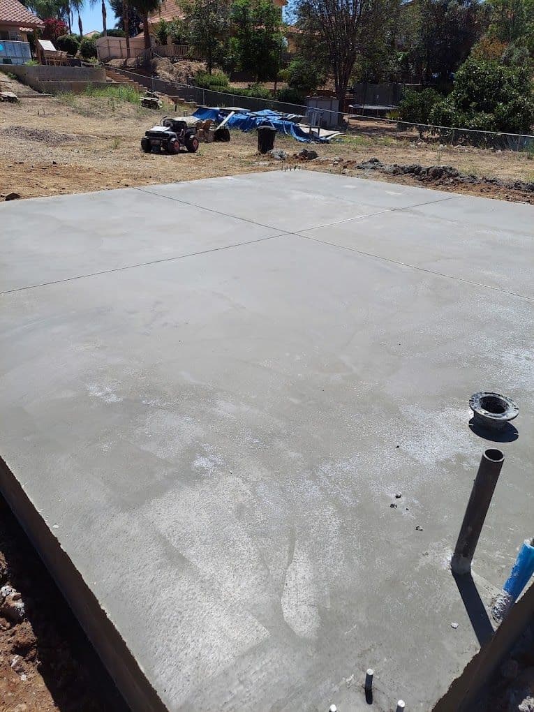 Concrete foundation slab installation in a residential yard, with tools and equipment nearby.