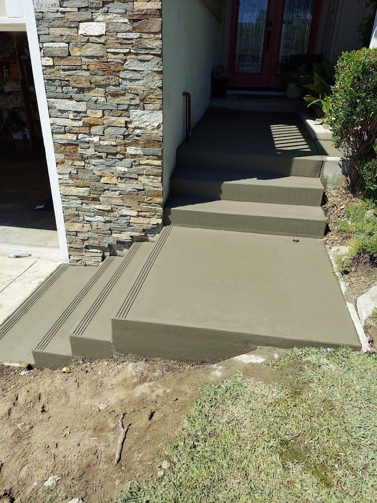Freshly poured concrete steps with textured surface and stone accents leading to a home entrance.