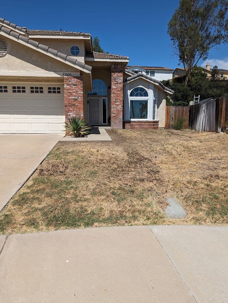 Single-story home with a brick entrance, garage, and sparse front yard under a clear blue sky.