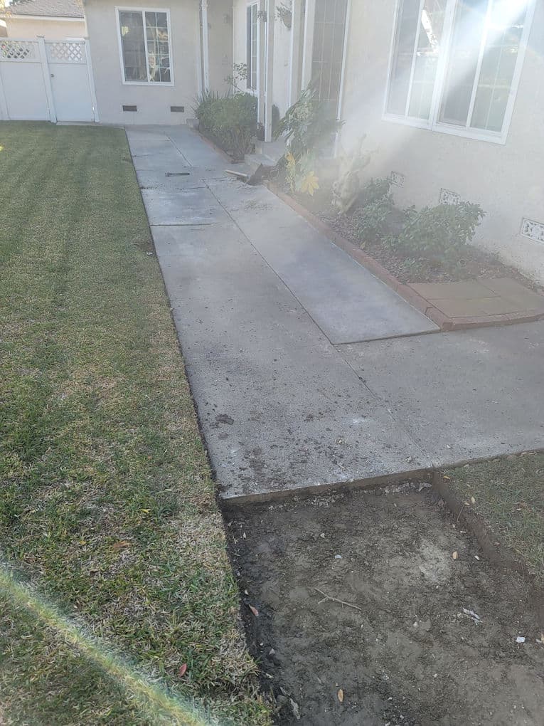 Concrete pathway leading to a house with lawn, showing recent landscaping work.
