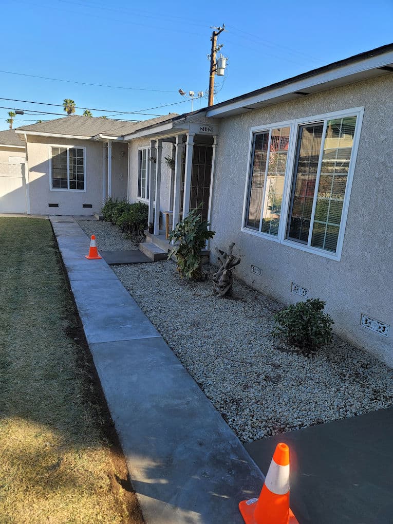 Newly landscaped home entrance with concrete walkway and decorative stones, featuring traffic cones.