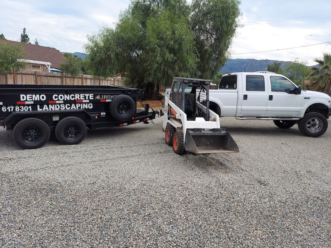 Bobcat skid steer with a trailer and pickup truck at a landscaping site. Concrete demo equipment.