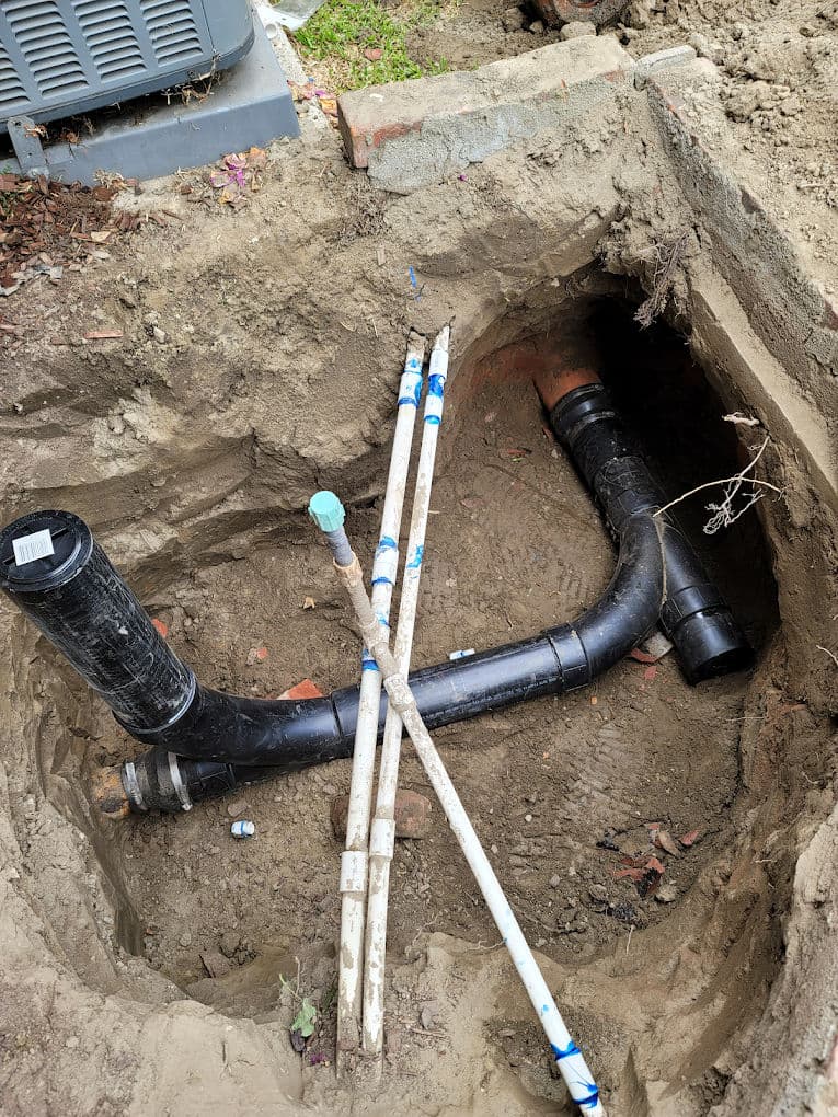 Exposed plumbing pipes and drainage system in a dug trench. Construction site details visible.