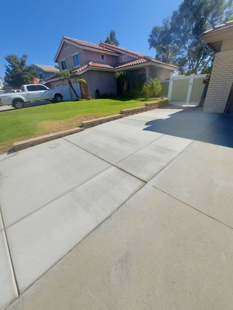 Residential driveway and lawn with a house in the background, clear blue sky overhead.