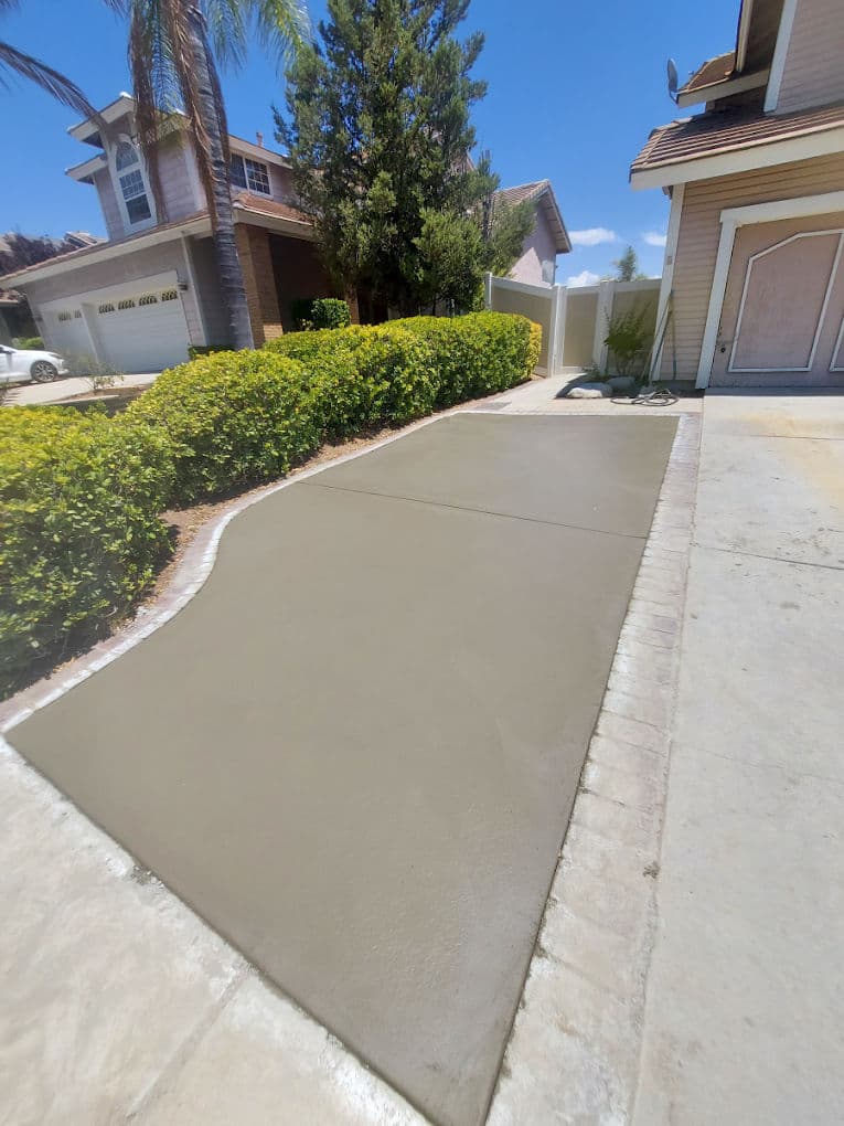 Freshly poured concrete driveway in a residential neighborhood with green shrubs and palm trees.