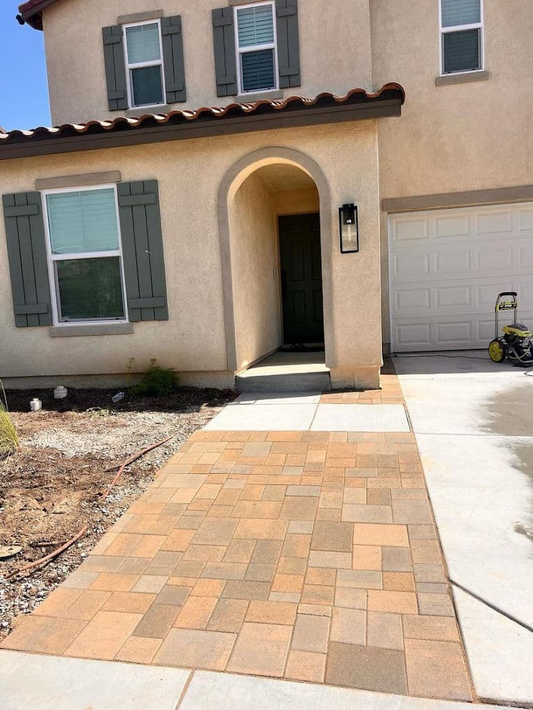 Newly paved walkway leading to a residential front door with gray shutters and garage.