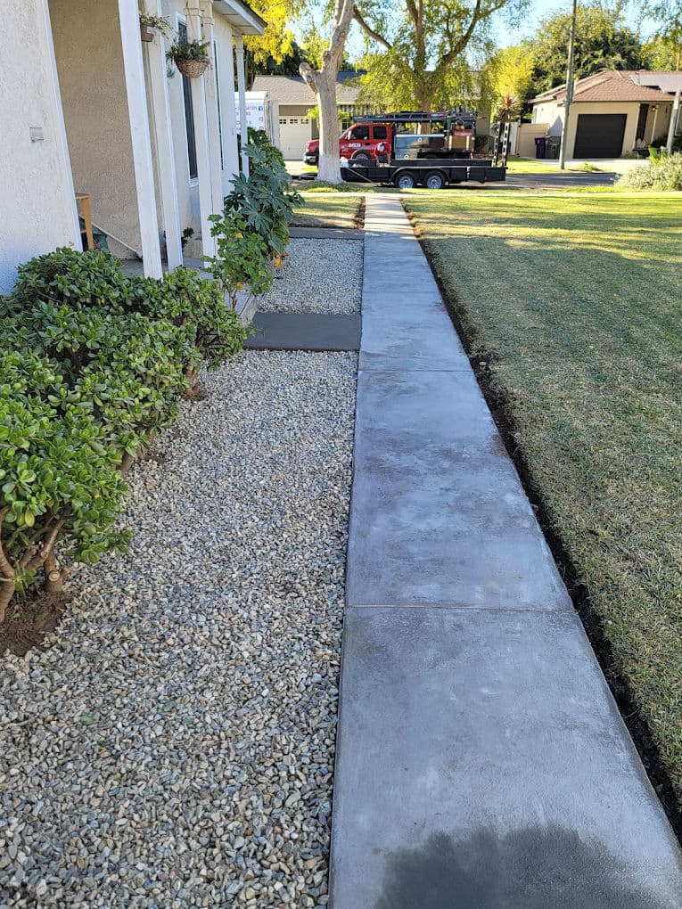 Concrete walkway alongside gravel and shrubs, enhancing landscaping appeal in sunny neighborhood.