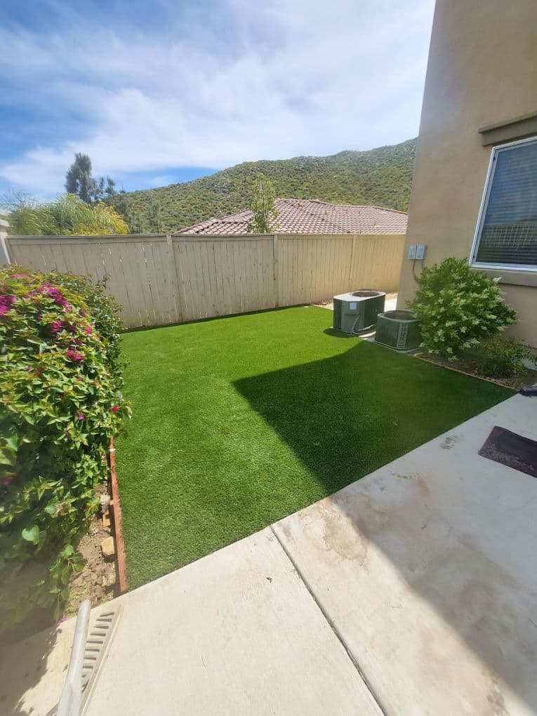 Lush green artificial lawn in a residential backyard with air conditioning units and mountain view.