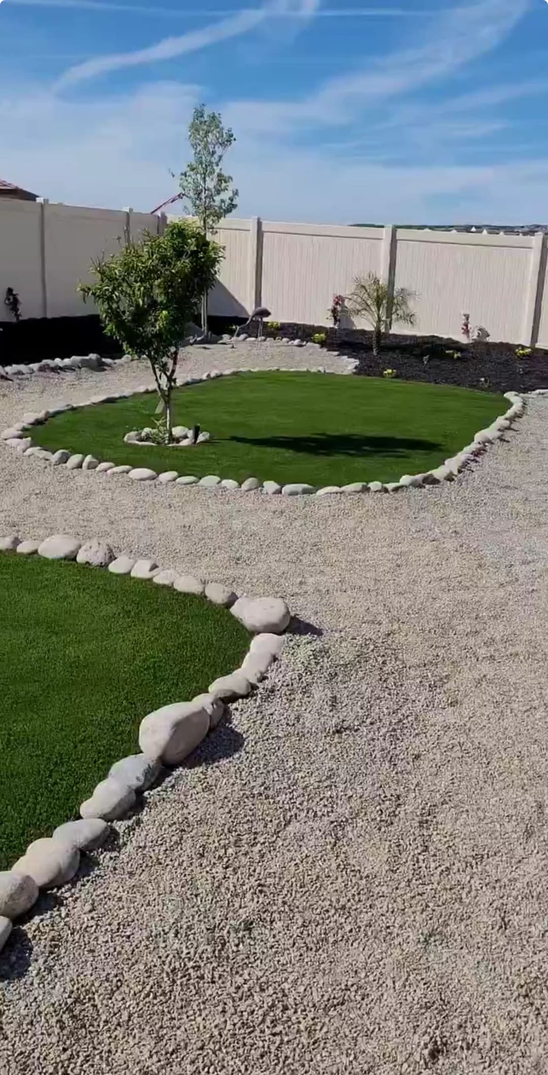 Landscaped garden with green grass, decorative rocks, and a small tree under a blue sky.