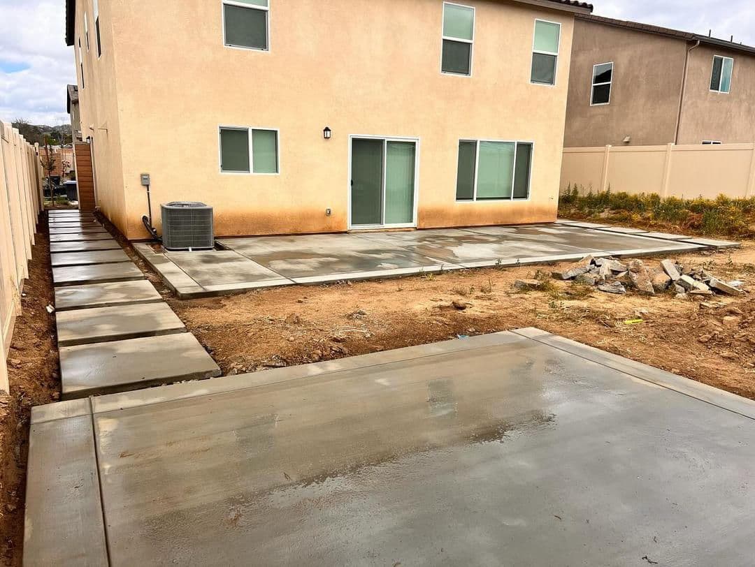 Freshly poured concrete patio and walkway behind a house, with a beige exterior and air conditioning unit.