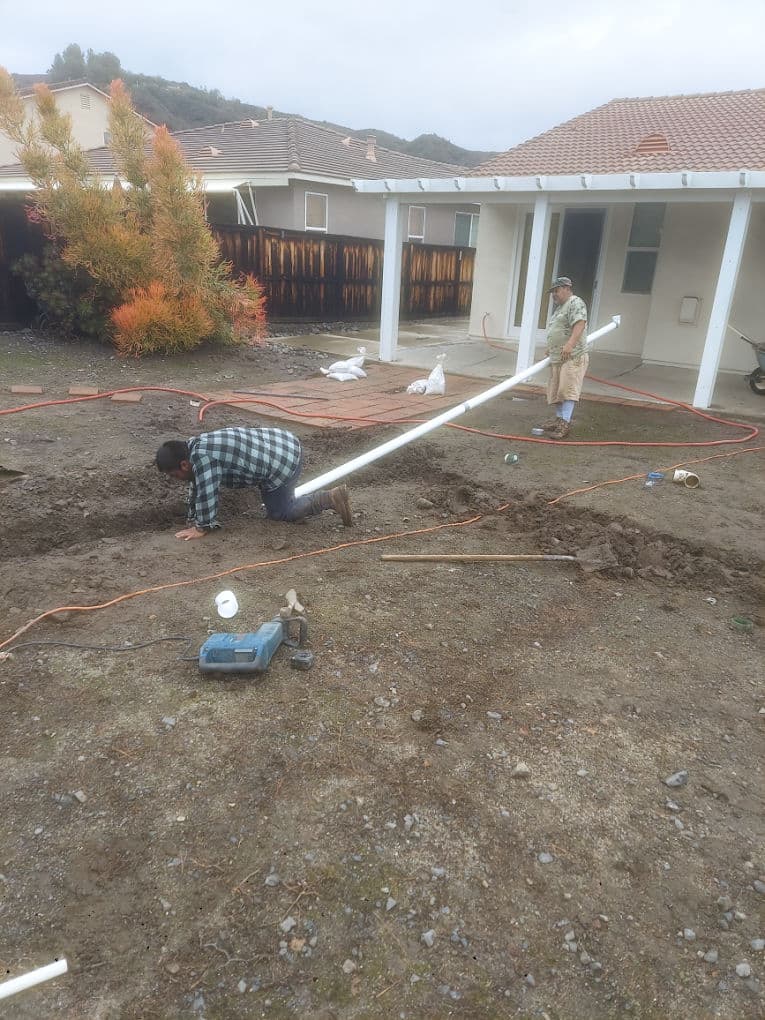 Workers installing plumbing in a backyard, digging trenches and handling pipes for irrigation.