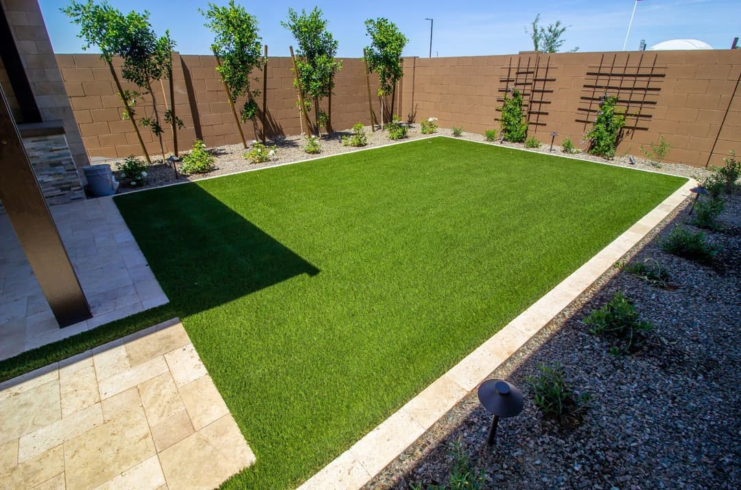 Lush green artificial turf lawn surrounded by decorative gravel and plants in modern backyard.