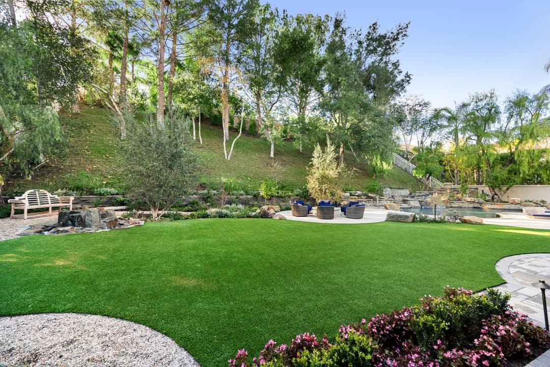 Lush green lawn with landscaped trees and seating area in a serene outdoor garden.