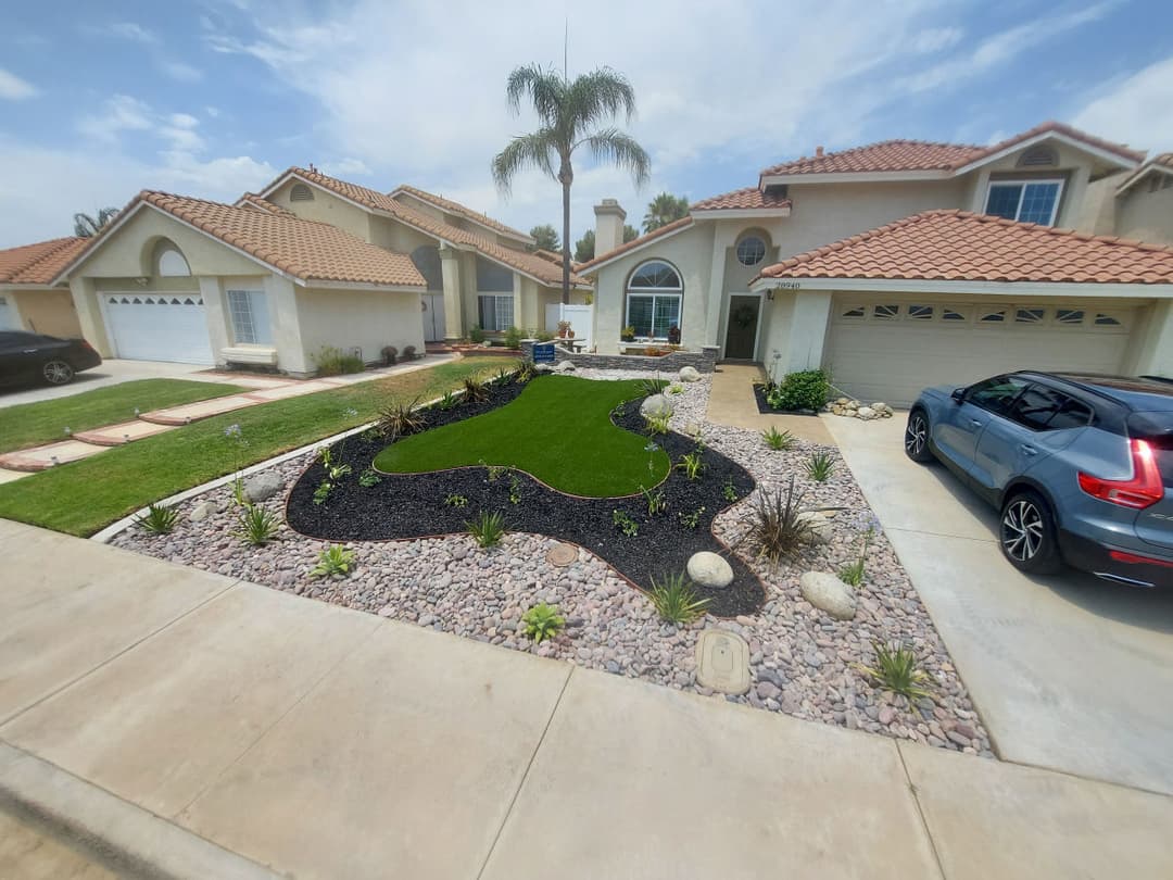 Modern front yard landscaping with curved grass, rocks, and plants near a stylish home.