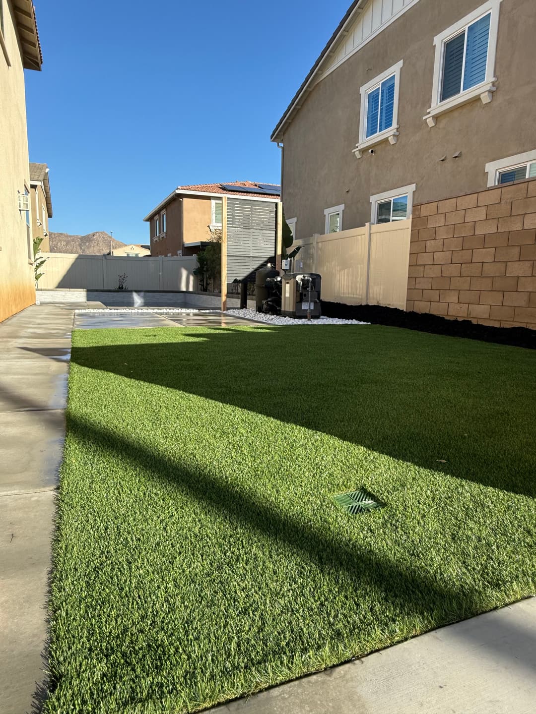 Lush green artificial turf backyard with modern landscaping and clear blue sky.