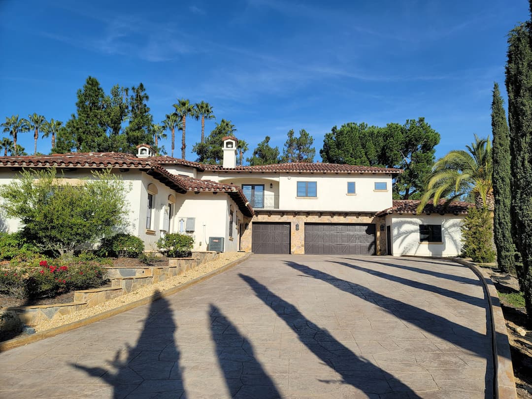 Luxury Mediterranean-style home with lush landscaping and palm trees in clear blue sky.
