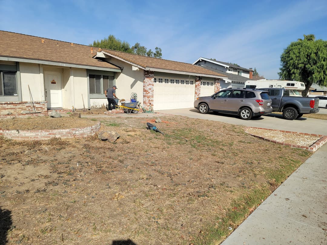 Home exterior with a freshly landscaped yard, a man gardening, and parked vehicles.