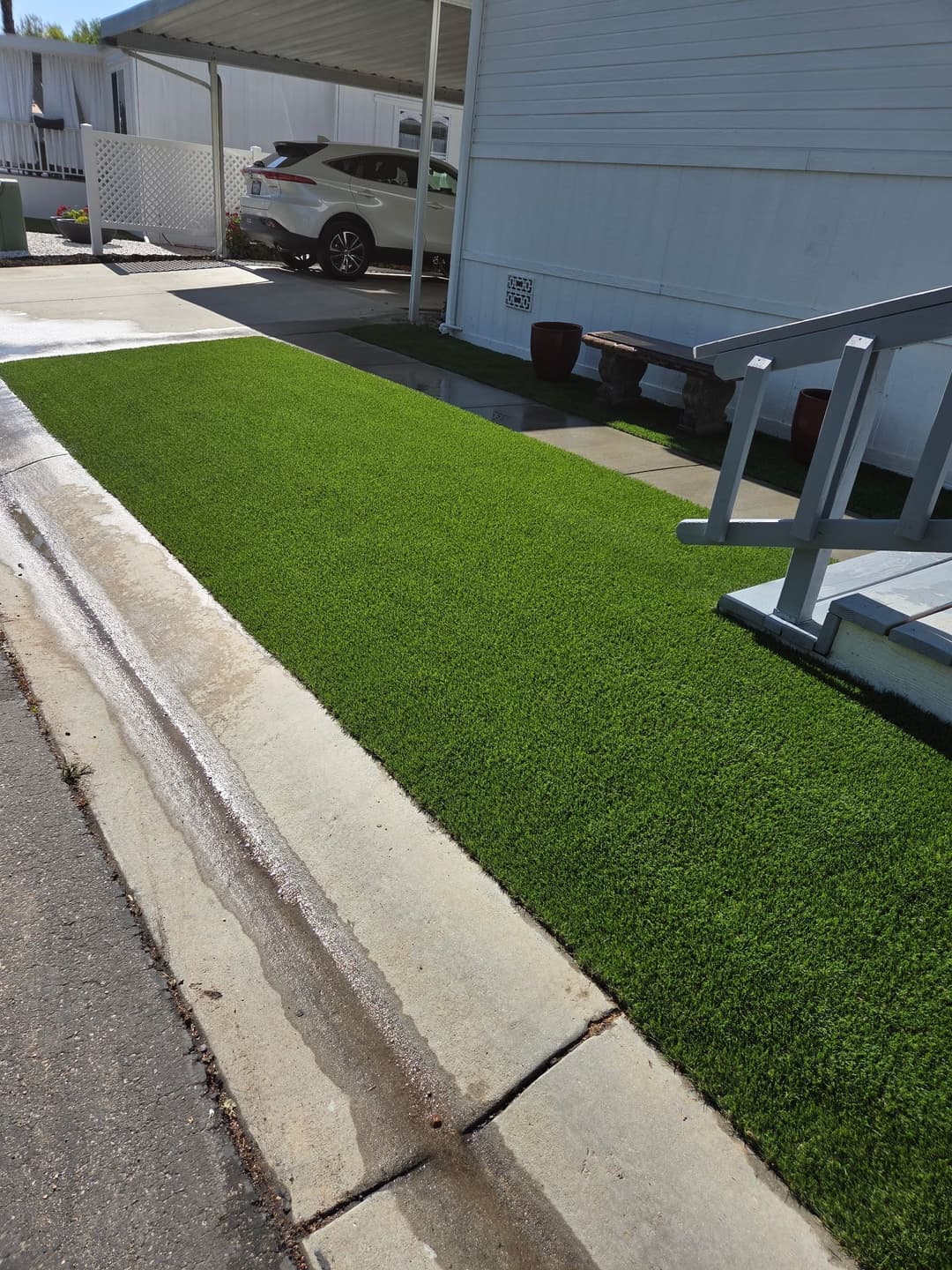 Lush green artificial turf next to a paved driveway and car, enhancing outdoor space.