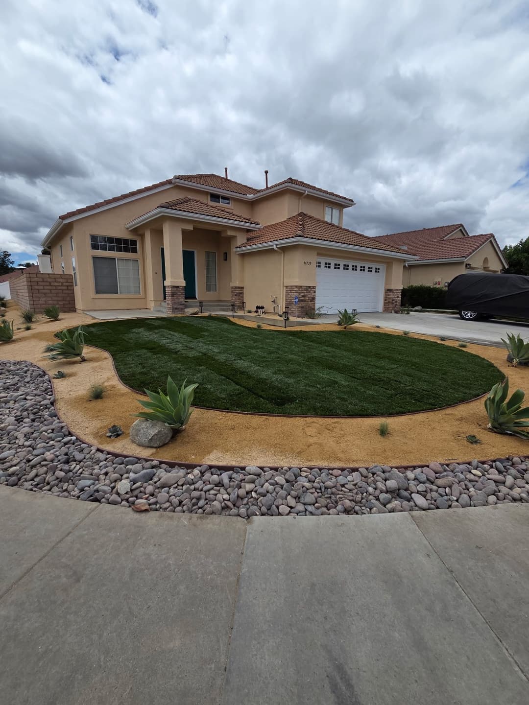 Modern home with a lush green lawn, desert landscaping, and cloudy sky.