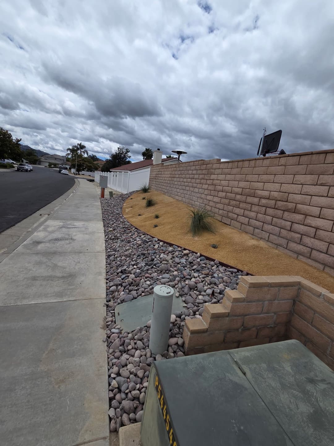 Desert landscape design with decorative stones, low plants, and a wall alongside a sidewalk.