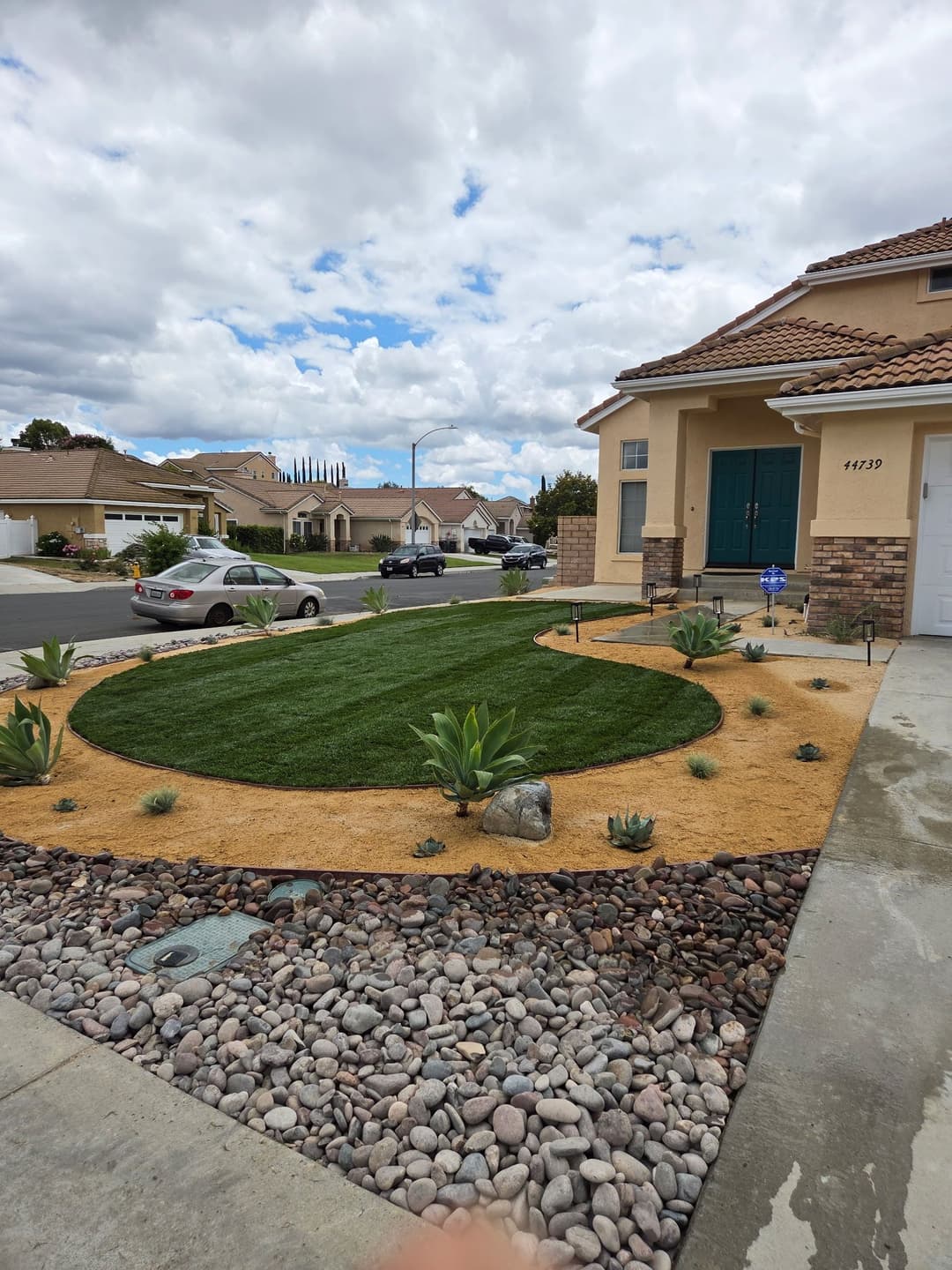 Residential front yard with lush green lawn, desert plants, and decorative gravel.