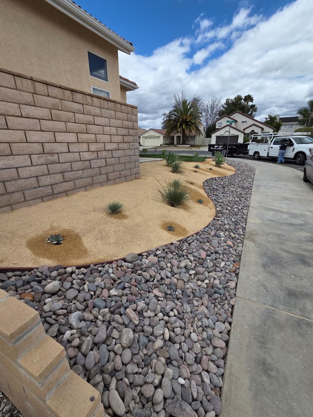 Desert landscape design with rocks, sand, and drought-resistant plants beside a house.