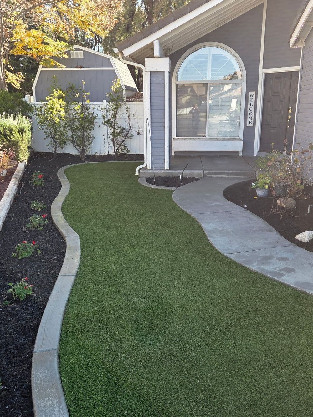 Lush green artificial grass pathway leading to a welcoming home's entrance with flower beds.