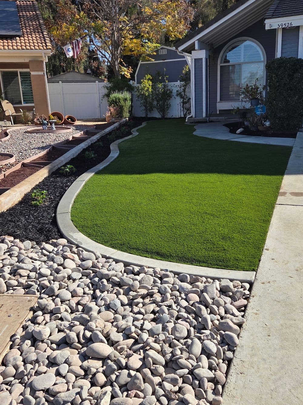 Lush green artificial turf lawn with decorative stones and landscaped path outside a home.