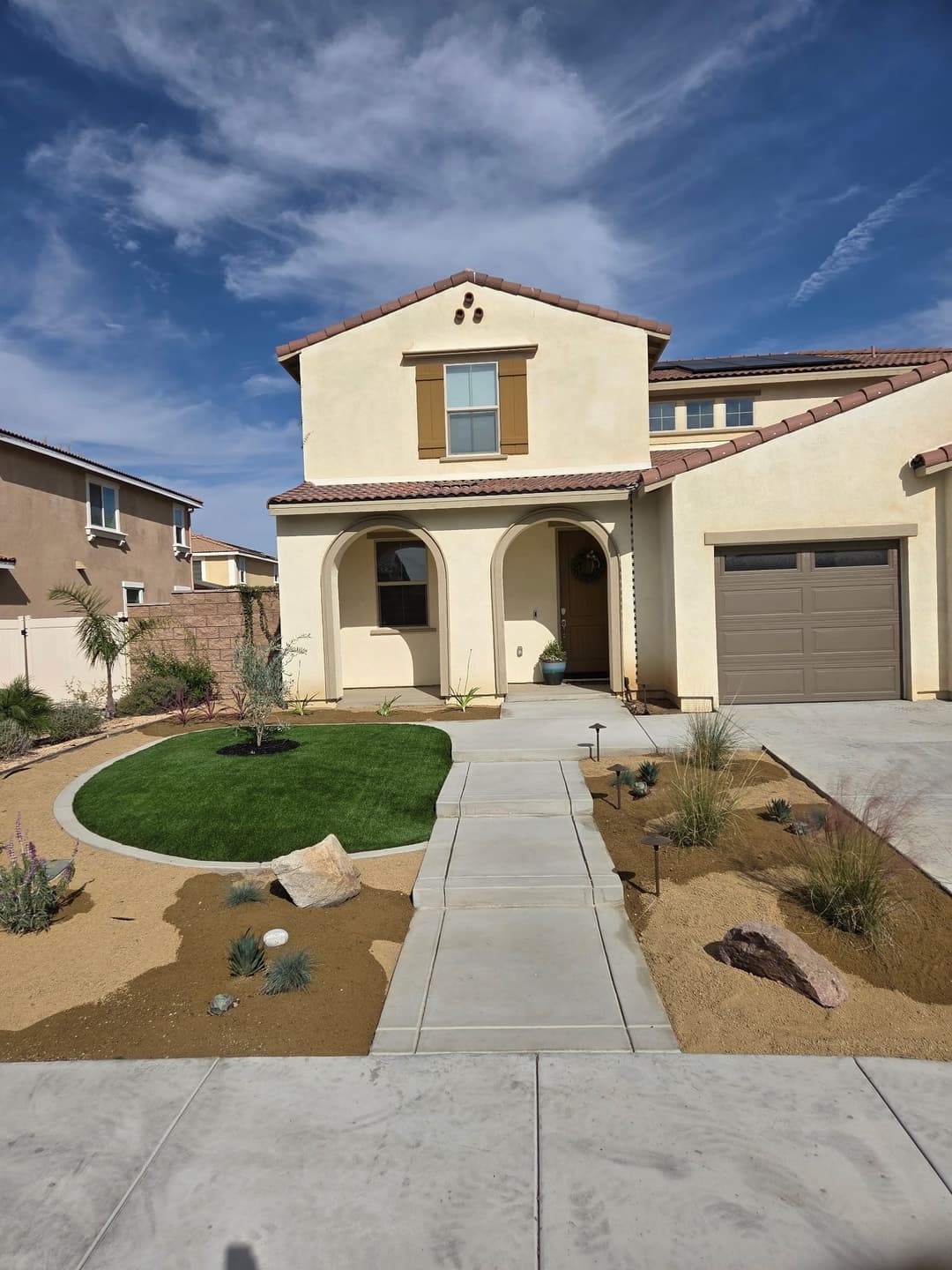 Modern two-story home with a landscaped front yard and blue sky in the background.
