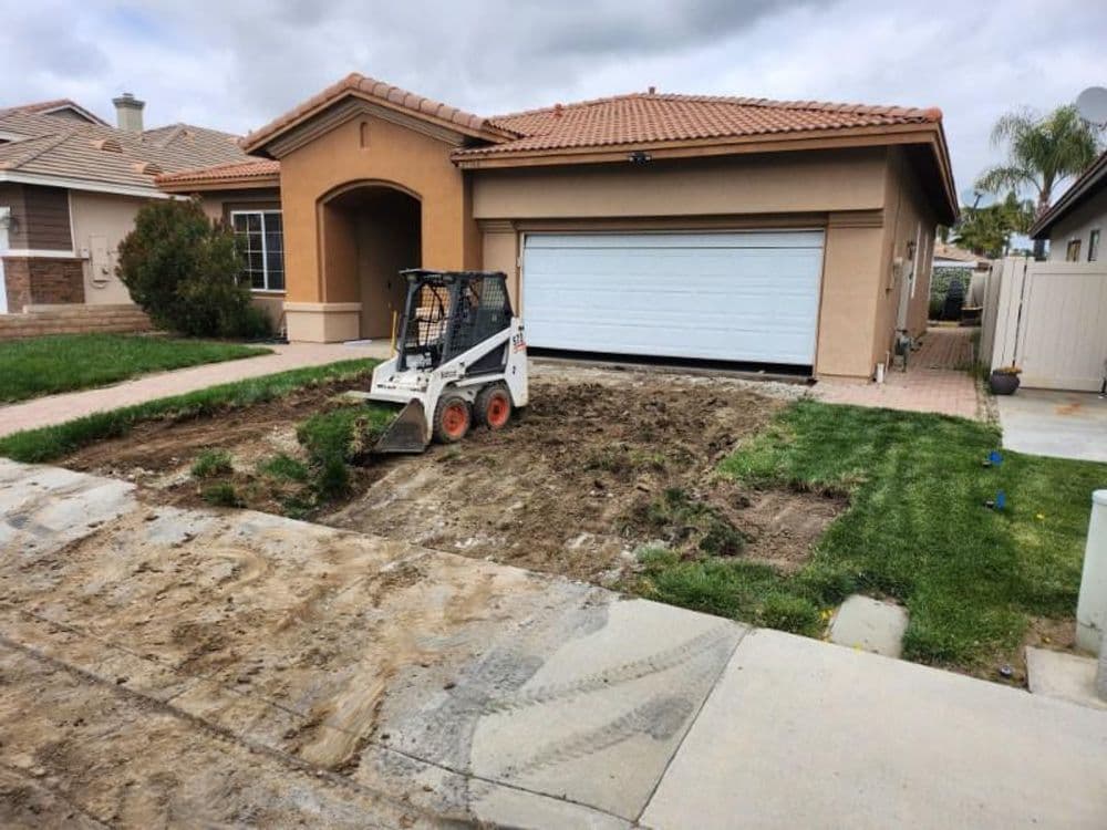 Bobcat loader parked in a residential yard undergoing landscaping changes near a garage.