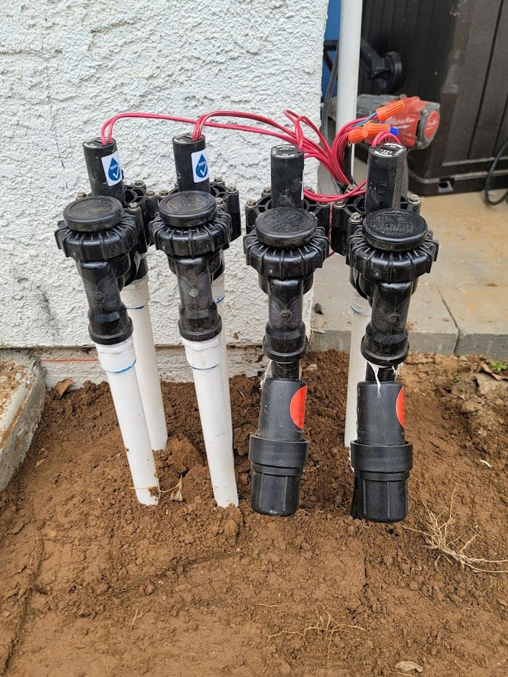 Irrigation control valves with PVC pipes and wires, installed in a garden area.