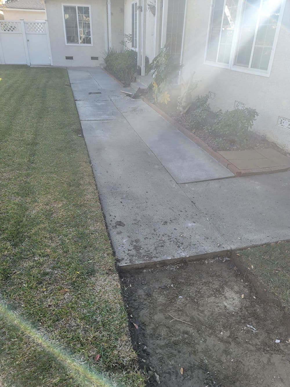 Residential walkway under construction with freshly poured concrete and grassy lawn.