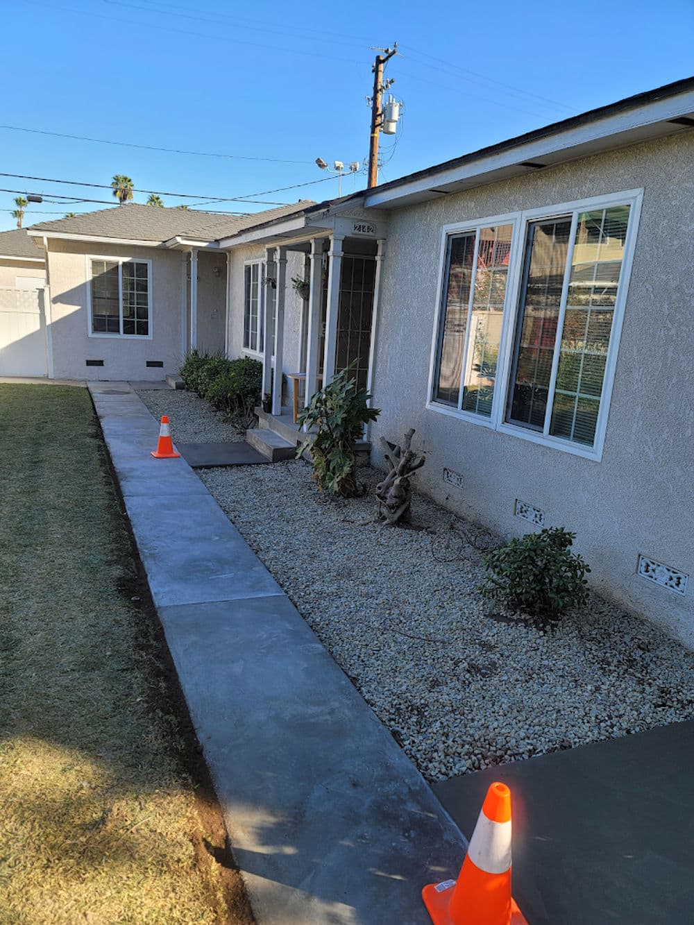 Home exterior with landscaped garden, concrete walkway, and safety cones. Sunny day.